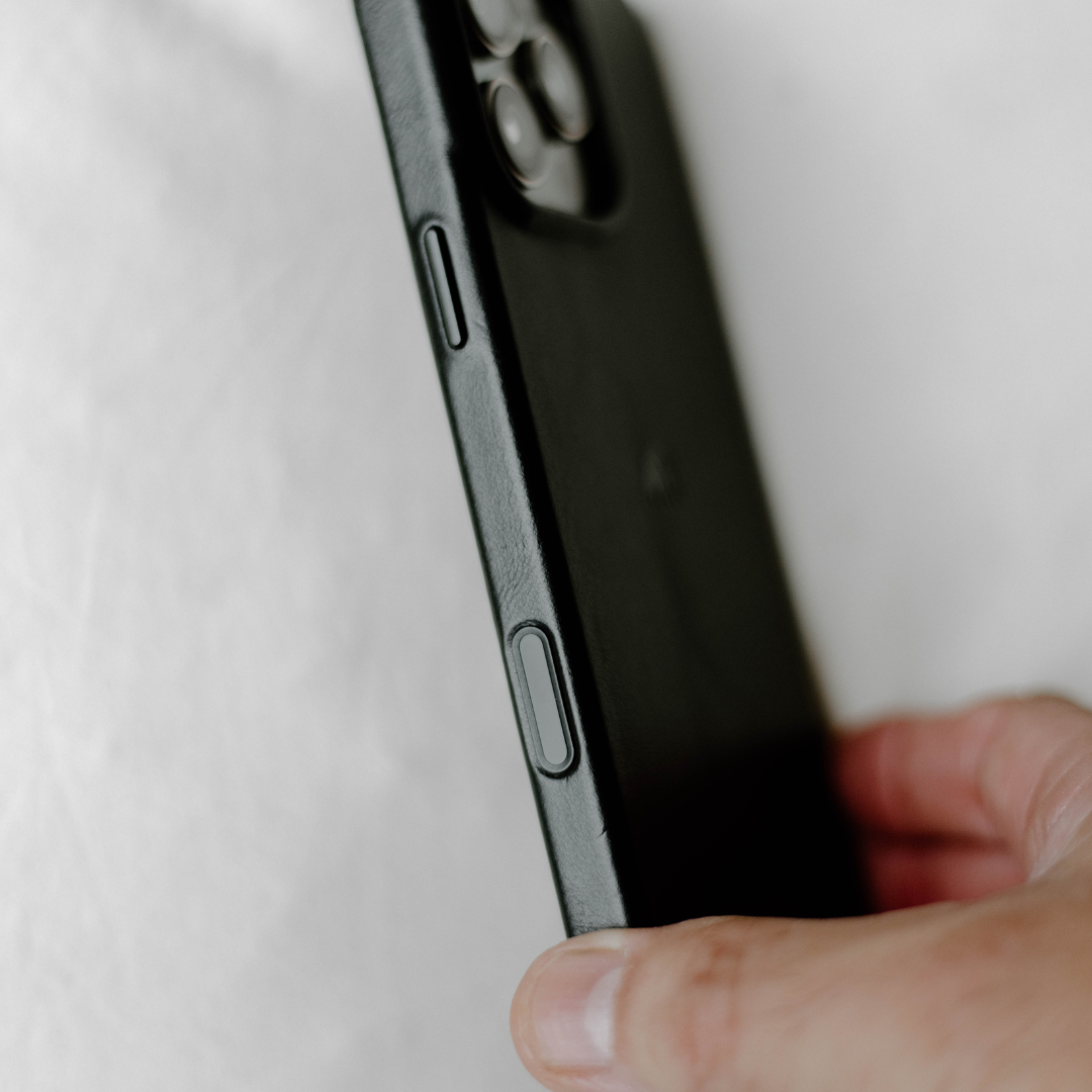 Close-up side view of a black minimalist phone case showing the button cutout and a thumb holding the edge