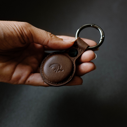 Hand holding brown leather keychain case with round tracker and metal key ring, embossed elephant logo