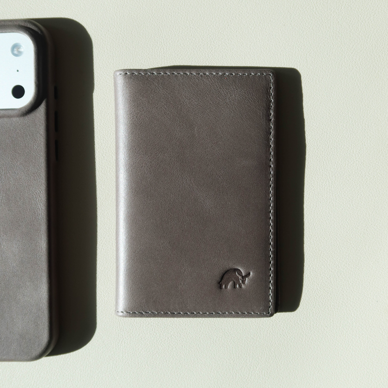 Dark brown leather card wallet with small embossed Bullstrap logo on light textured background; phone case edge at left