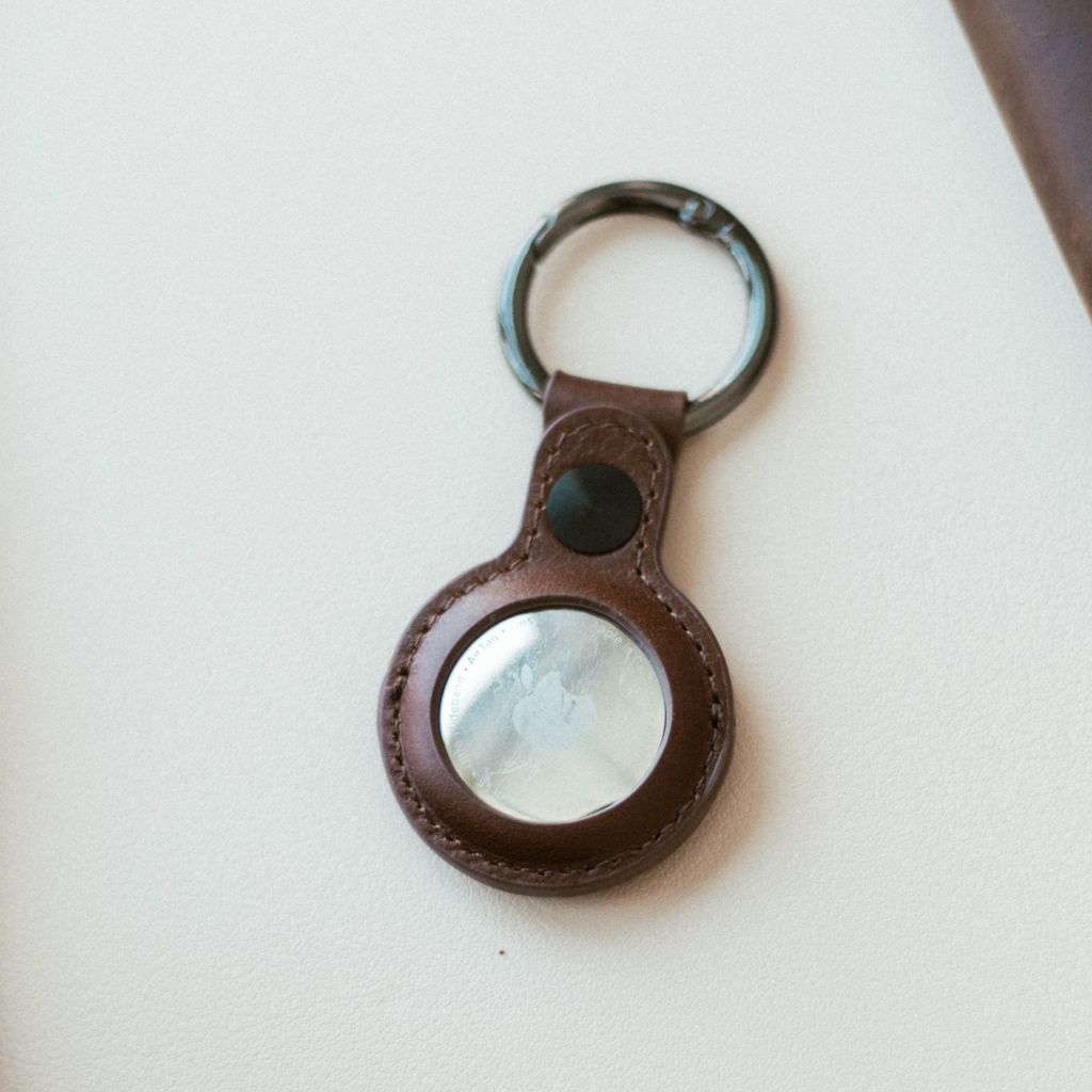 Brown leather keyring with attached Apple AirTag — round silver reflective disc and metal split ring.