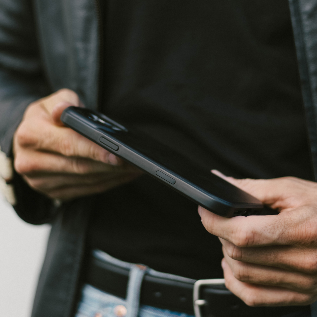 Black Flex phone case held in both hands against a person wearing a black shirt and jeans, showing case side buttons.