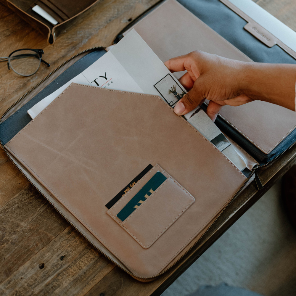 A person placing documents into a leather MacBook sleeve with card slots, showcasing its functionality.