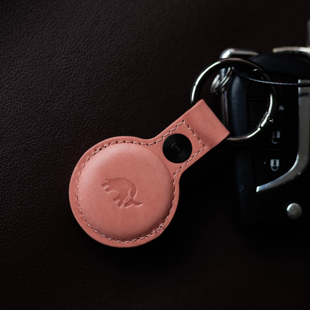 A pink leather AirTag holder attached to a keychain on a dark surface.