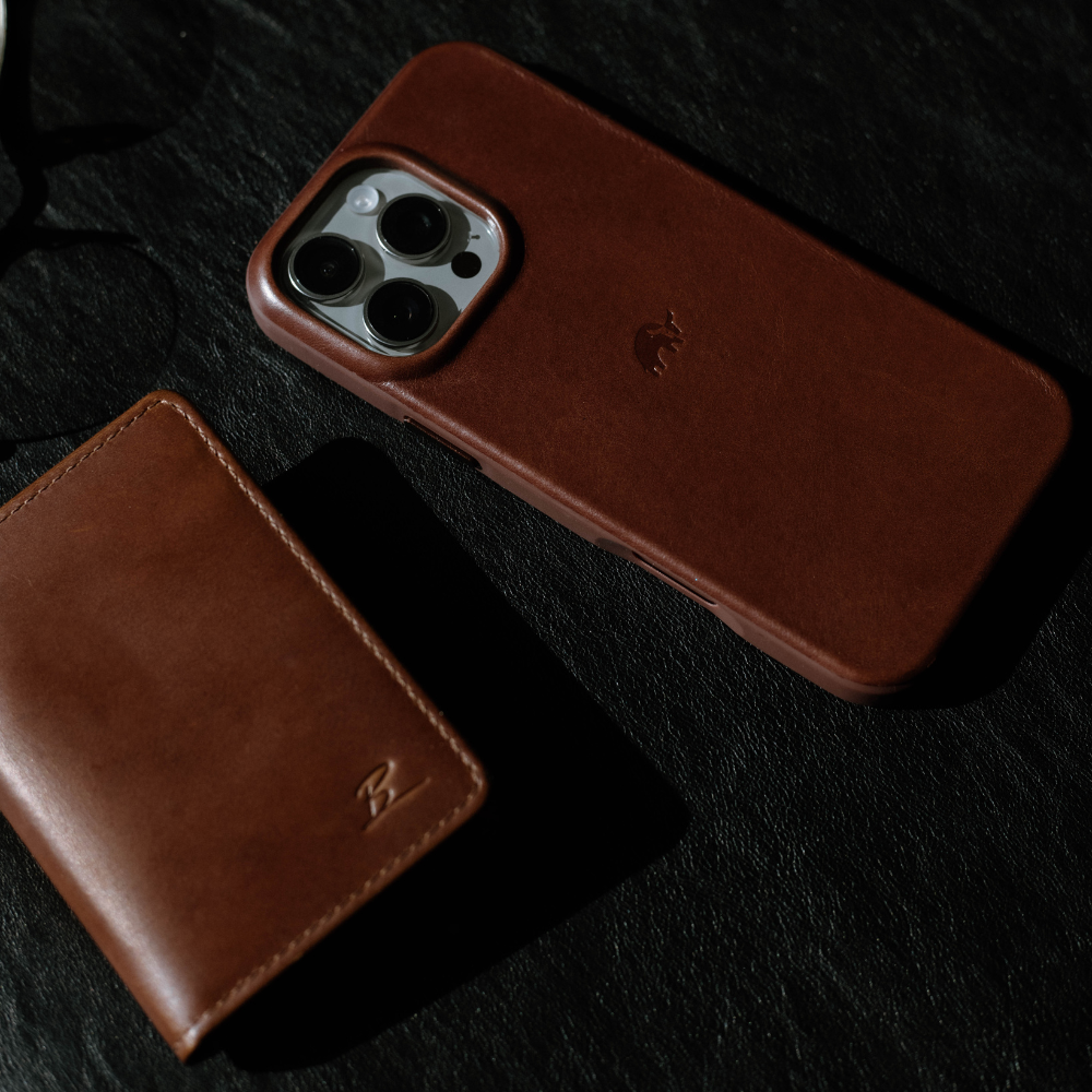 A brown leather iPhone case next to a matching wallet on a dark surface.