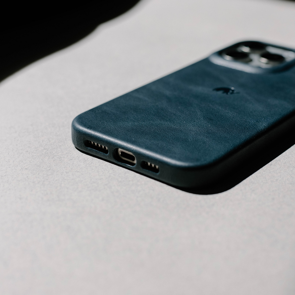 Ocean-blue leather smartphone case lying face down, showing charging port and dual-camera cutout.
