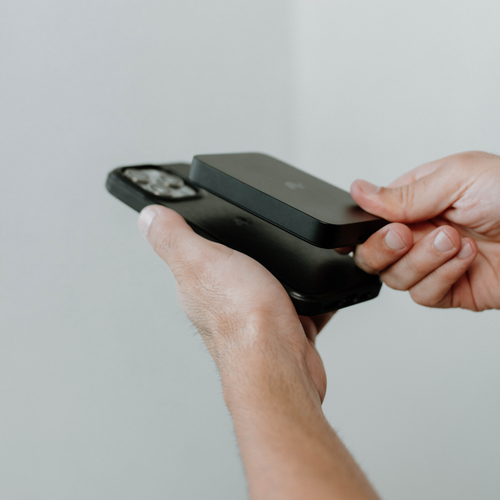 A person holding the MagSafe Power Bank above a smartphone, demonstrating its use.