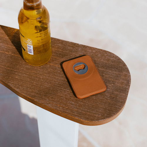 Sienna leather MagSafe wallet with round metal bottle opener on a wooden table beside a beer bottle