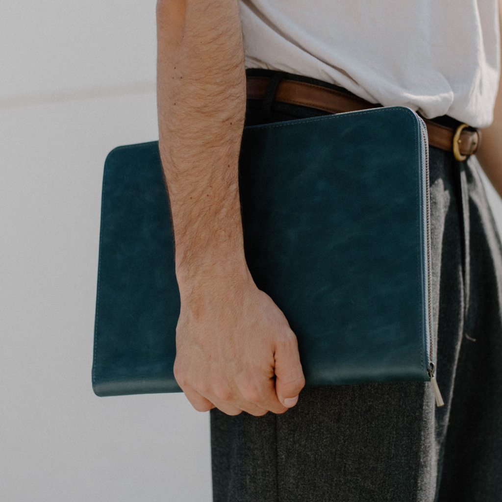 A person holding an ocean colored leather laptop sleeve, showcasing its design and color.