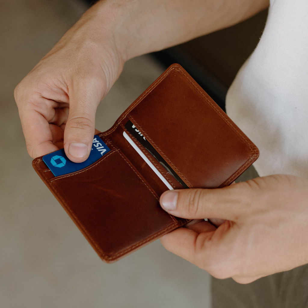 A person holding a brown leather wallet with a credit card inside.