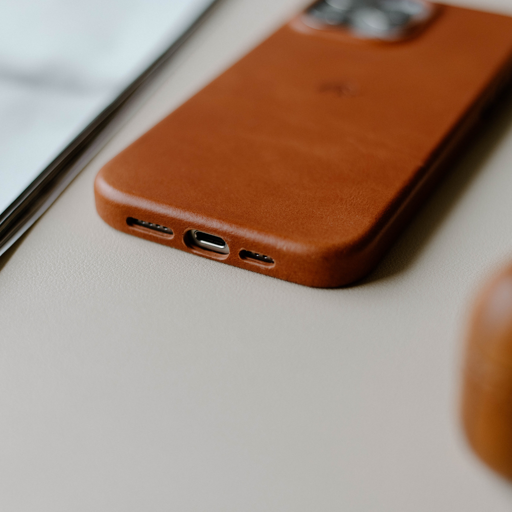 Sienna brown leather phone case lying face-down, showing bottom speaker and charging cutouts