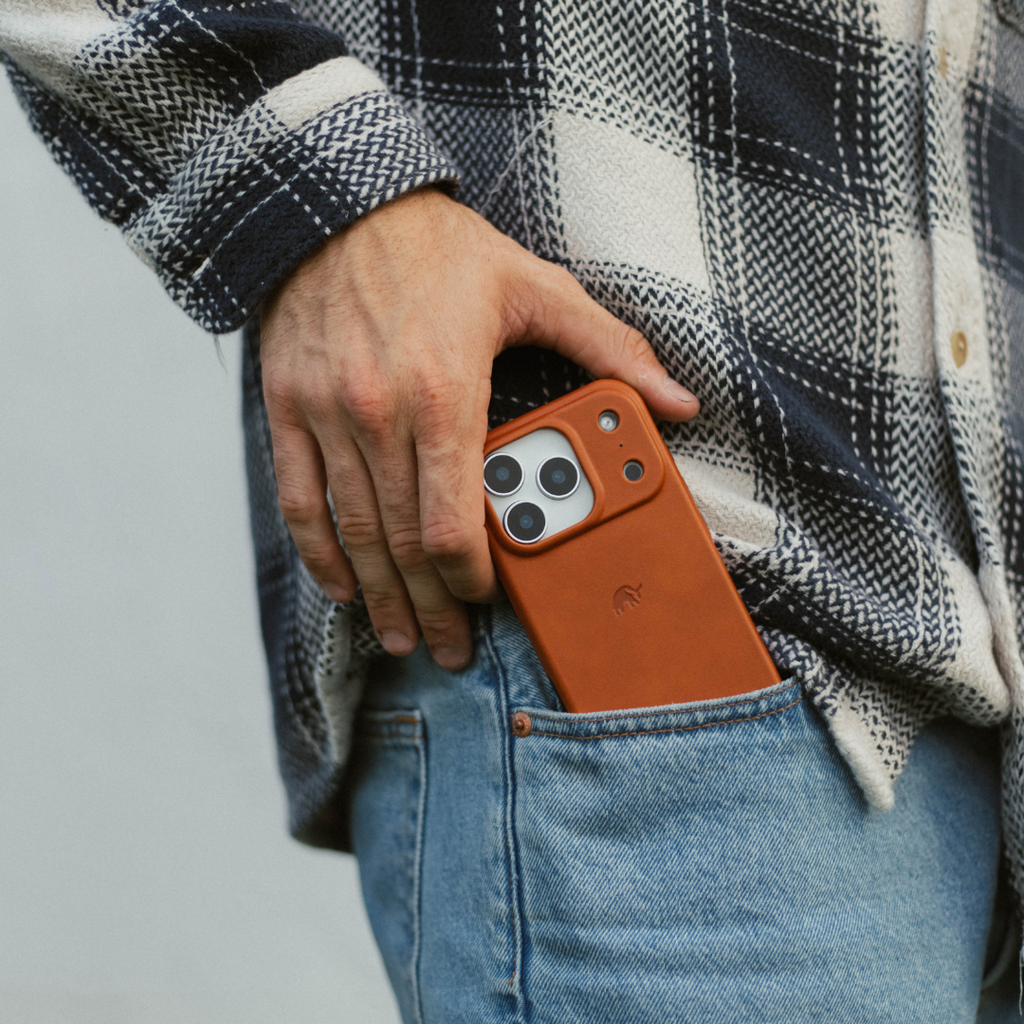 Brown leather iPhone case (sienna) being placed into a back jean pocket by a person wearing a plaid shirt