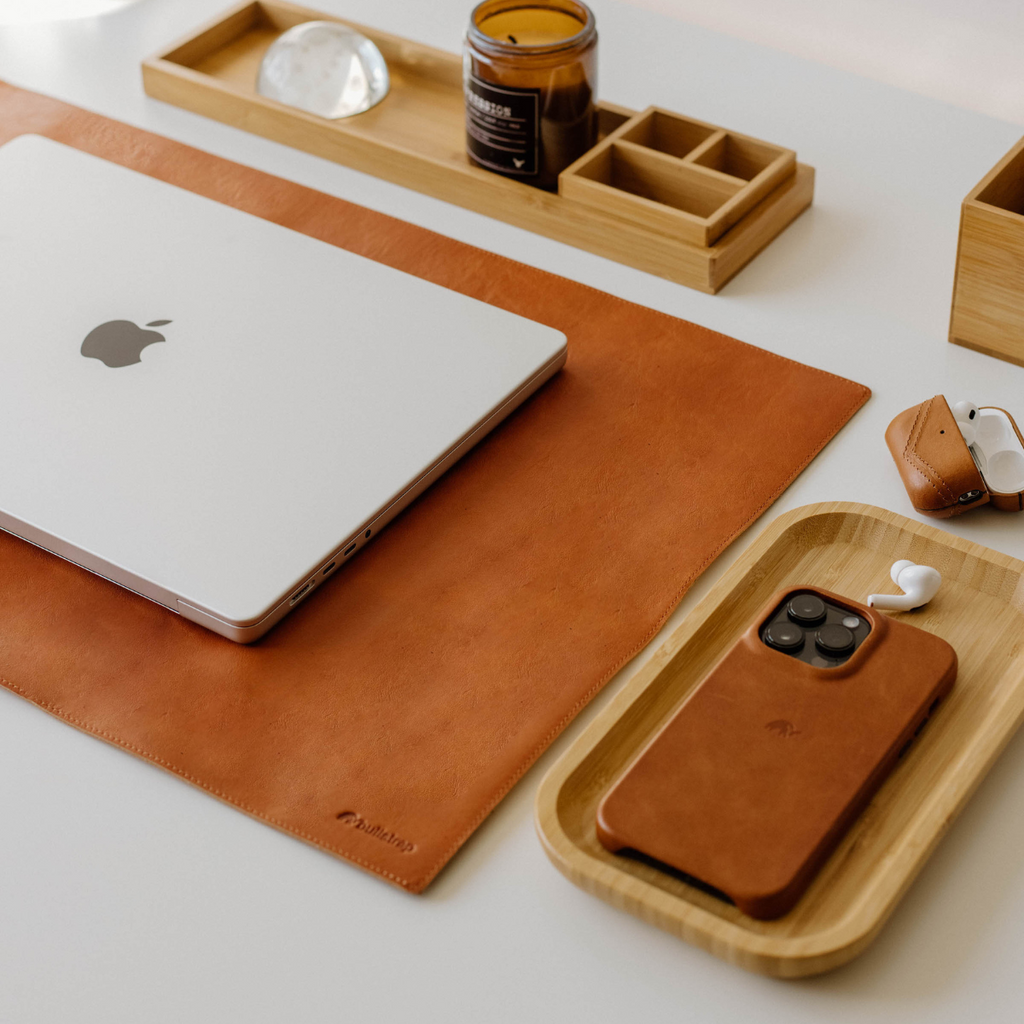 A leather desk mat in sienna color, with a laptop, phone, and accessories on a desk.