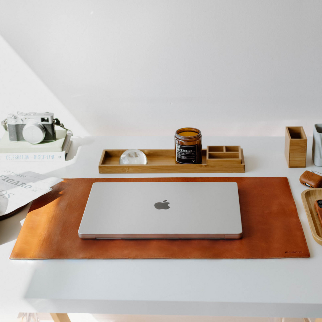 A leather desk mat in sienna color placed on a desk with a laptop and accessories.
