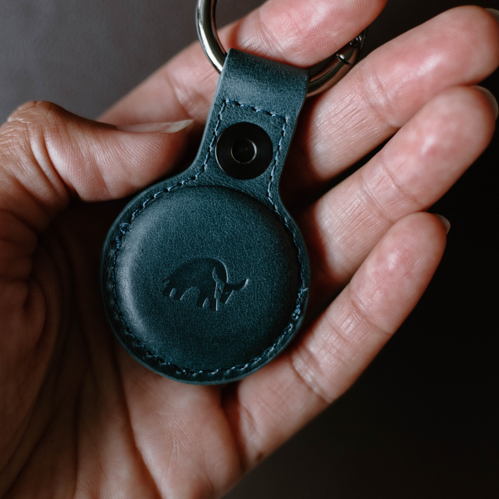 A hand holding a BullTag for AirTag in ocean color with a bull logo