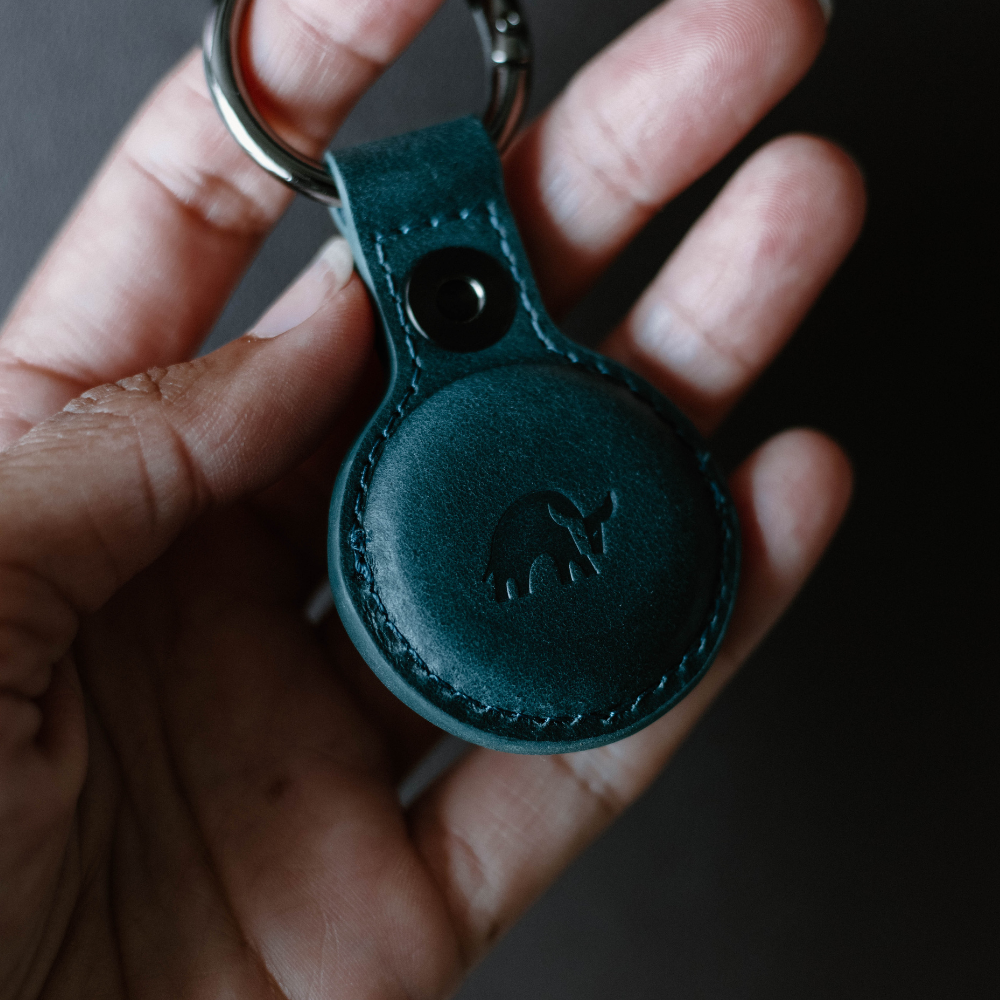 A hand holding a BullTag for AirTag in ocean color, featuring an embossed bull logo.