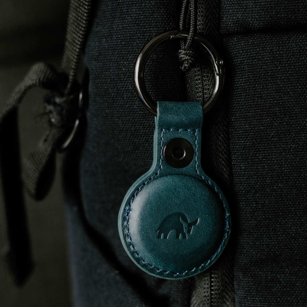 A teal leather BullTag for AirTag attached to a bag, featuring an embossed bull logo