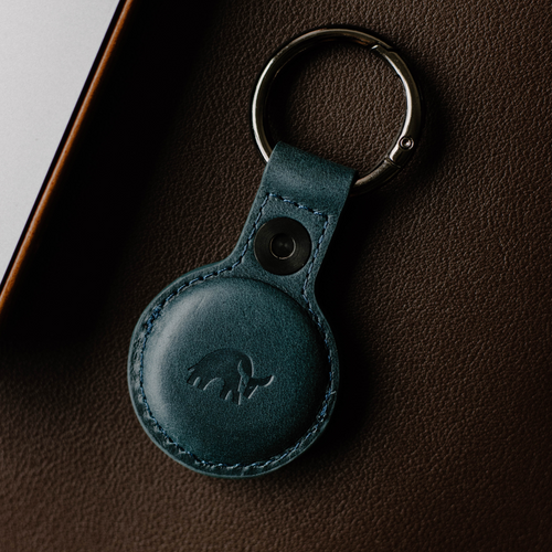 A teal leather AirTag holder with a keyring, featuring an embossed bull logo.