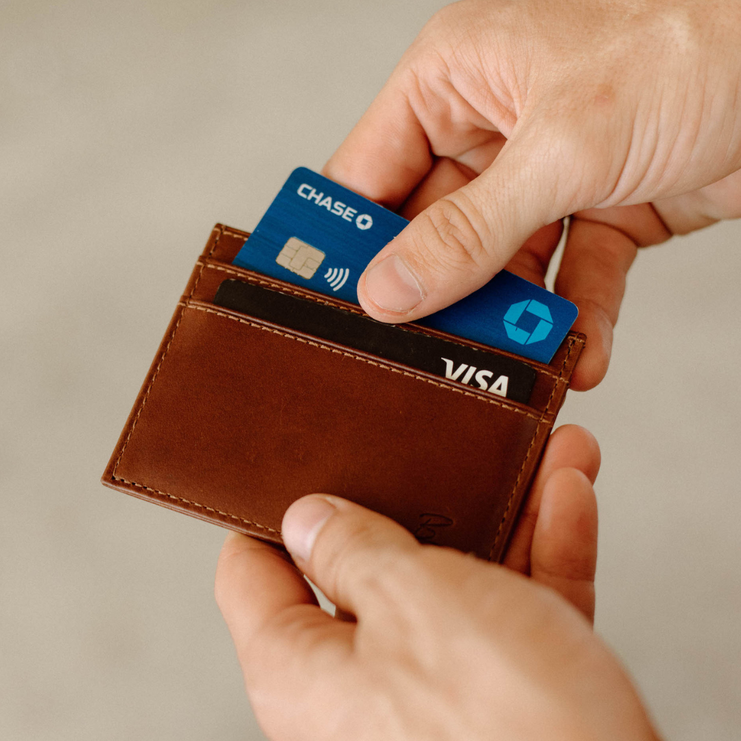 A person holding a brown leather wallet with cards visible.