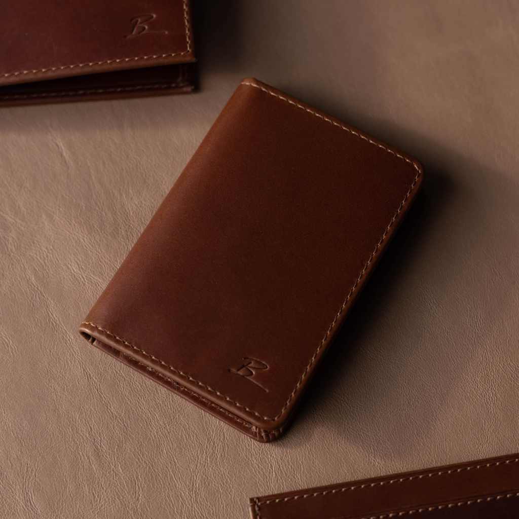 A brown leather wallet with a 'B' logo on a textured surface.