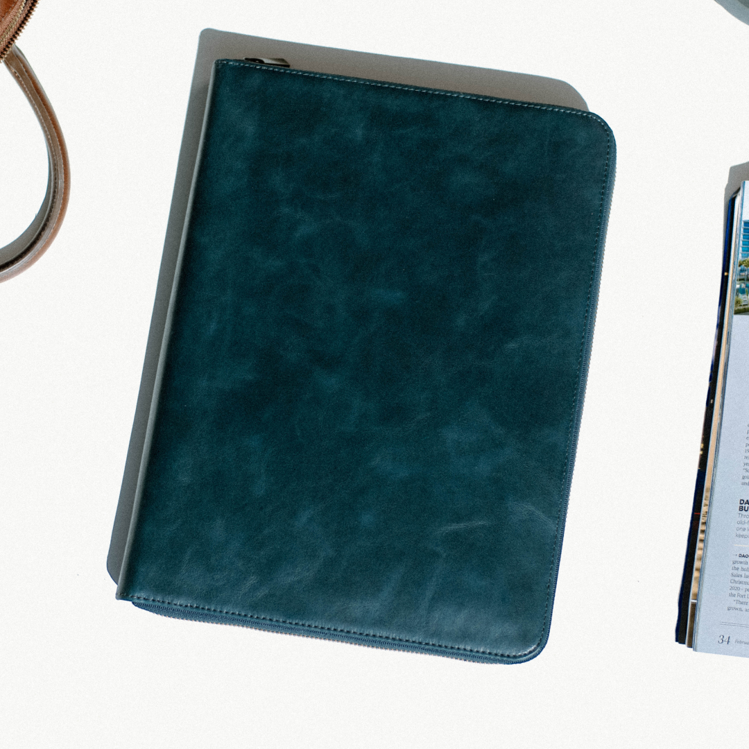 Teal leather zip folio on white table beside a magazine page showing "34"