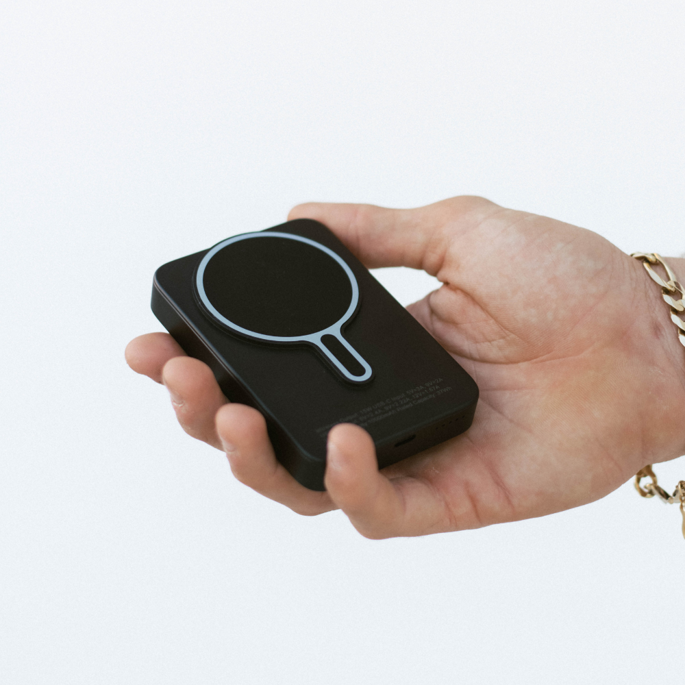 A hand holding a Bullstrap MagSafe Power Bank with a circular design on top.