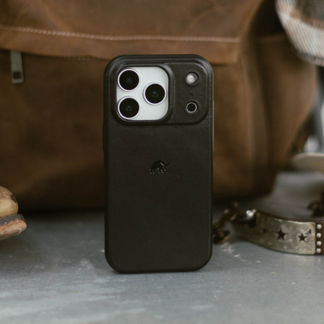 Black leather phone case with raised camera protector and triple-lens cutout, standing upright on a table