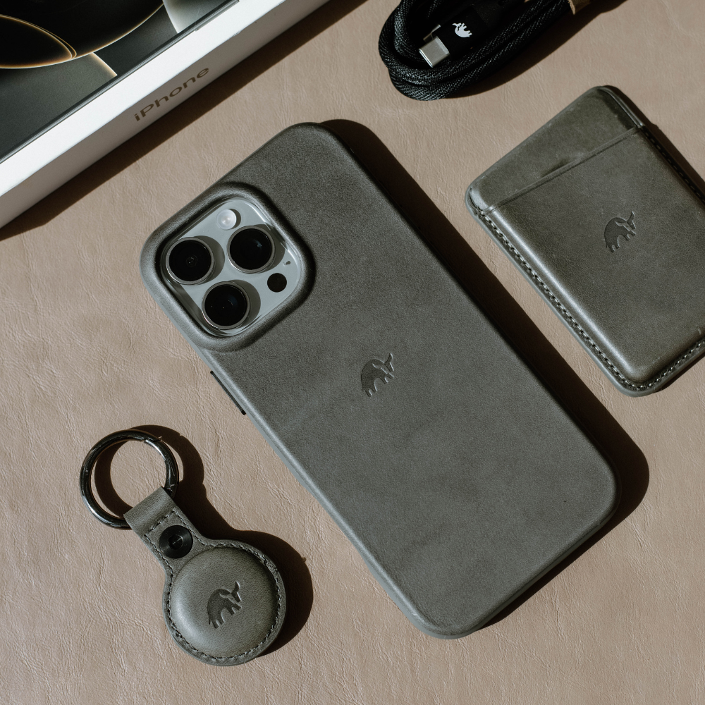 A gray leather iPhone case with a logo, a keychain, and a cardholder on a beige surface.