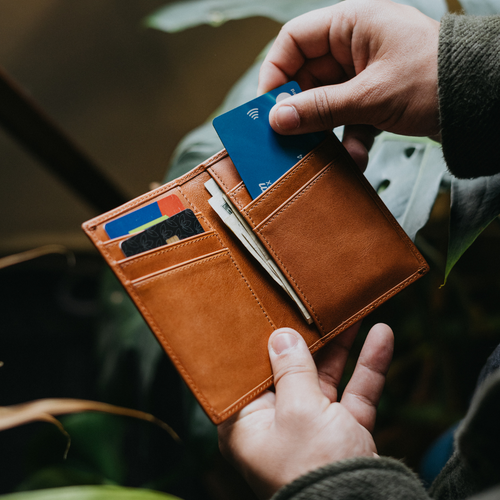 Sienna leather wallet held open in hands, showing card slots with cards and folded bills