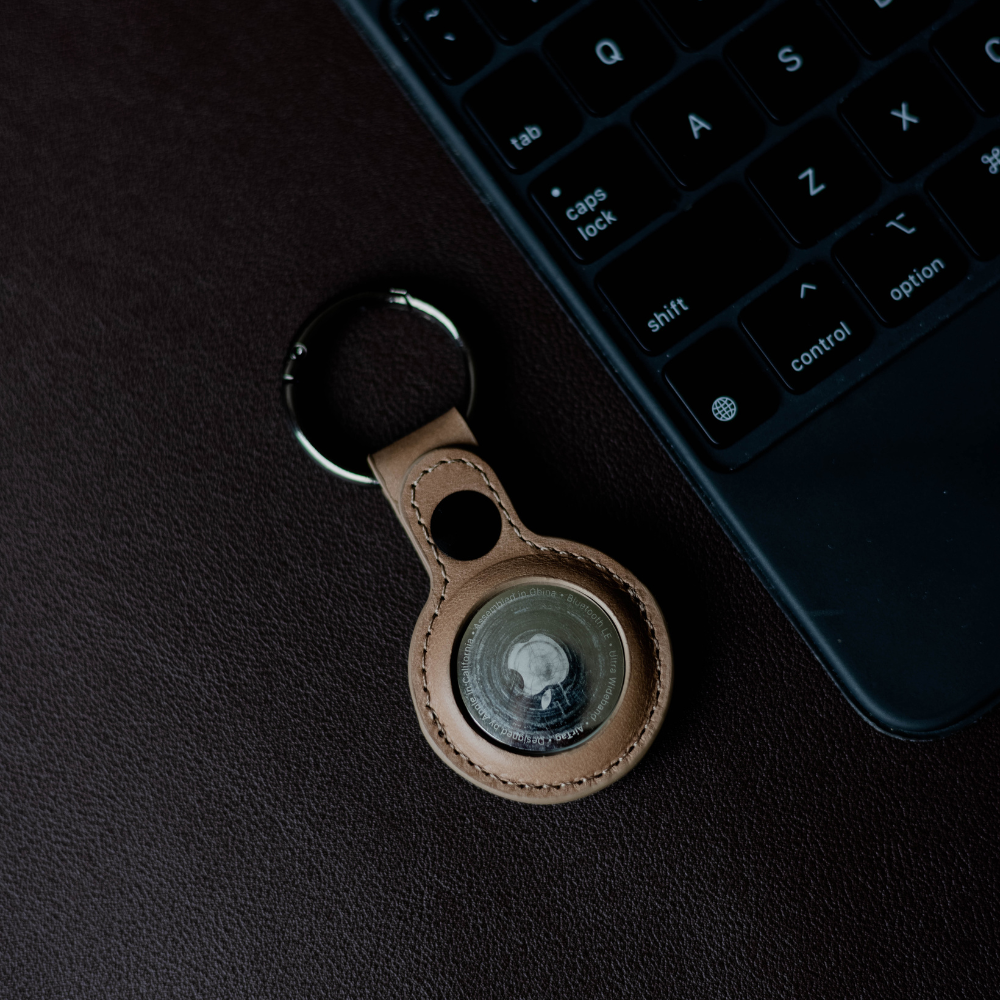 BullTag for AirTag in Dune color, featuring a keyring and AirTag holder on a brown surface next to a keyboard.