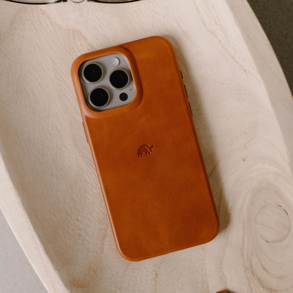Sienna leather iPhone case with embossed elephant logo resting on a light wooden tray