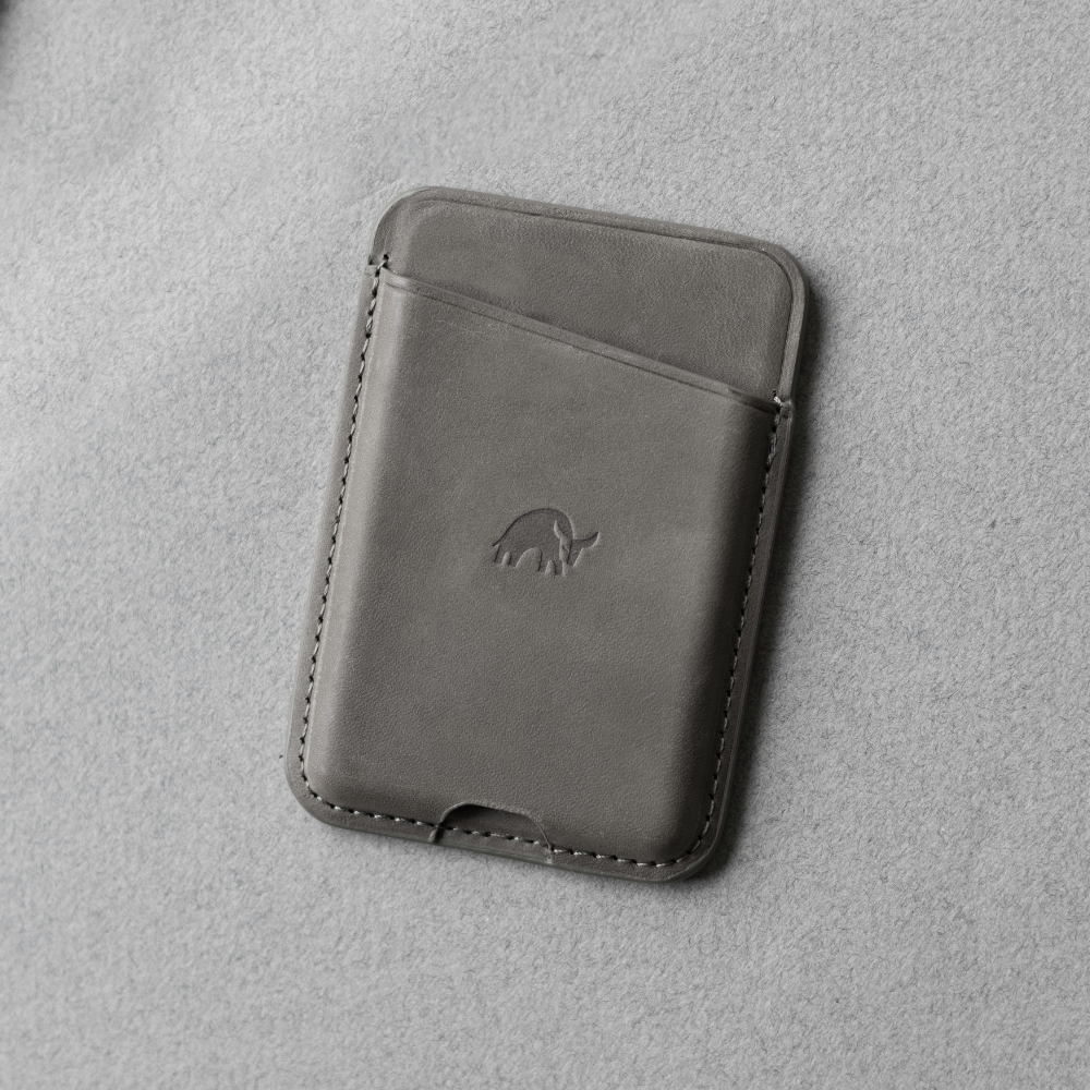 Slim gray leather card wallet with stitched edges and embossed anteater logo, single front card pocket on a felt surface.