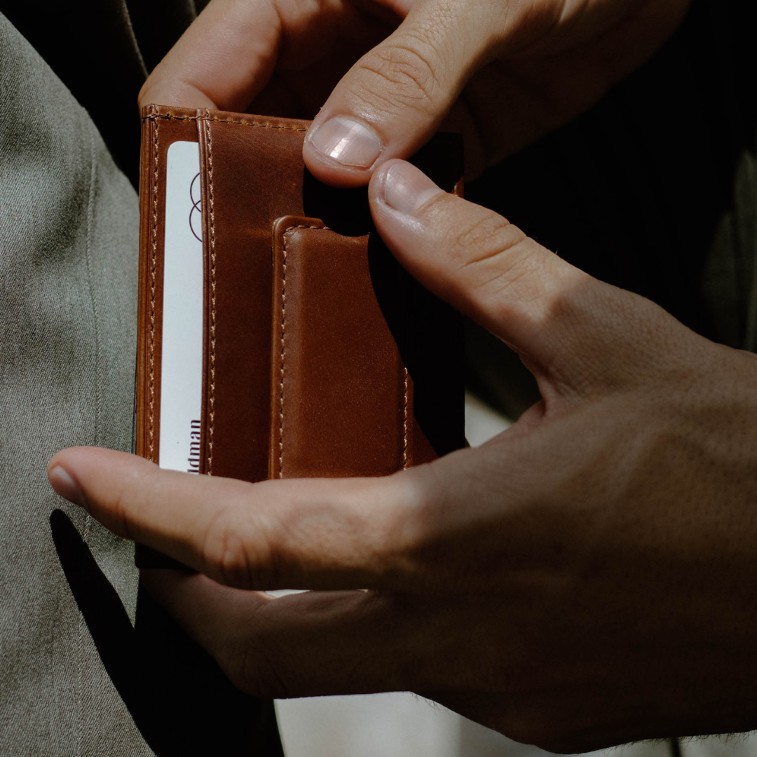 A person holding a Bullstrap Reserve - The Dealer money clip and card holder in cognac leather, showing the card slots.