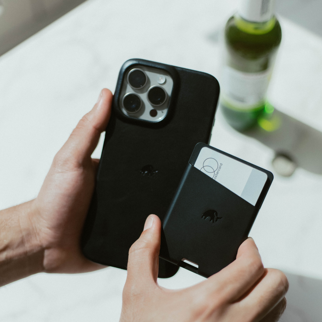 A person holding a black iPhone with a black Magnetic Popper Wallet attached, showcasing its design and functionality.