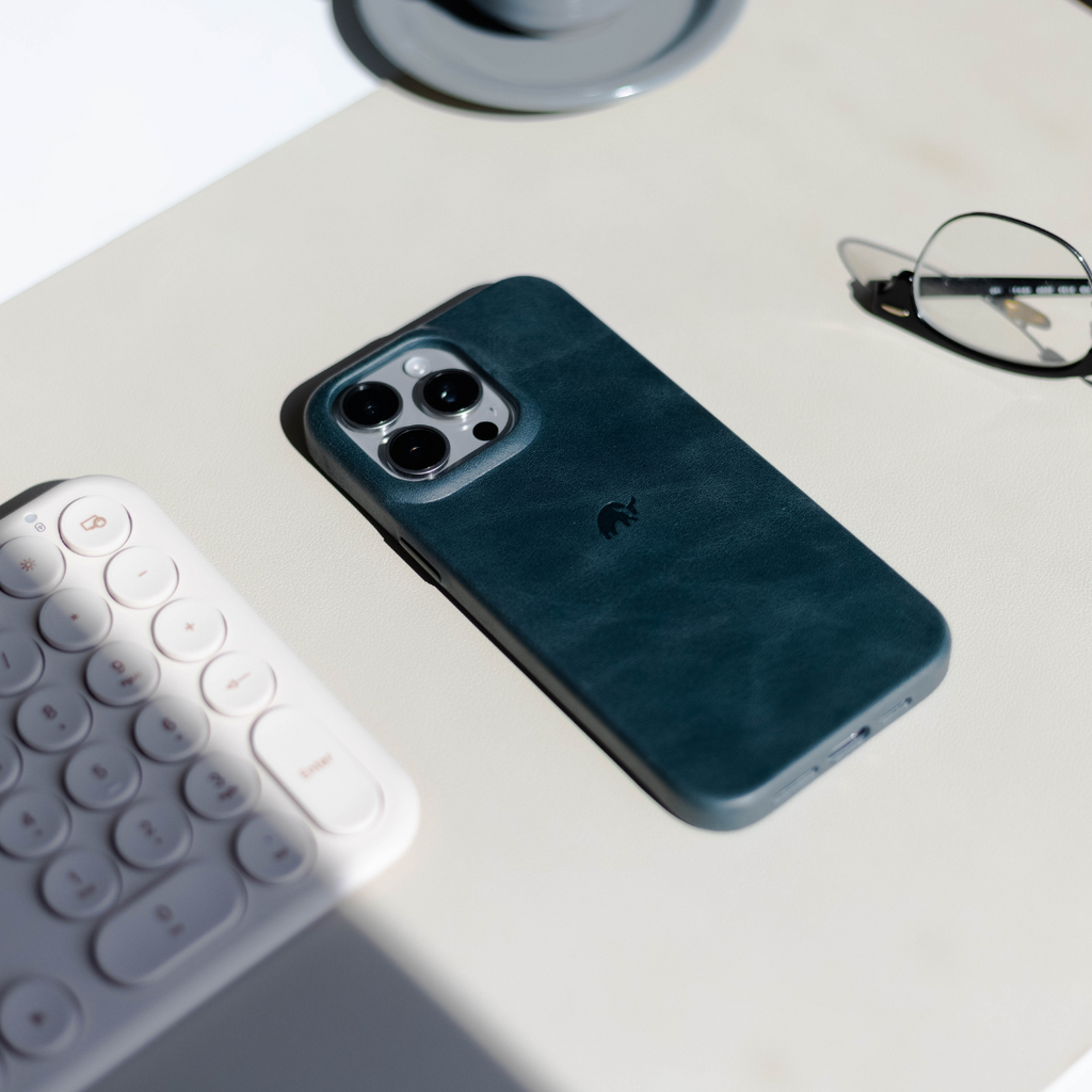 A teal phone case on a desk with a keyboard and glasses