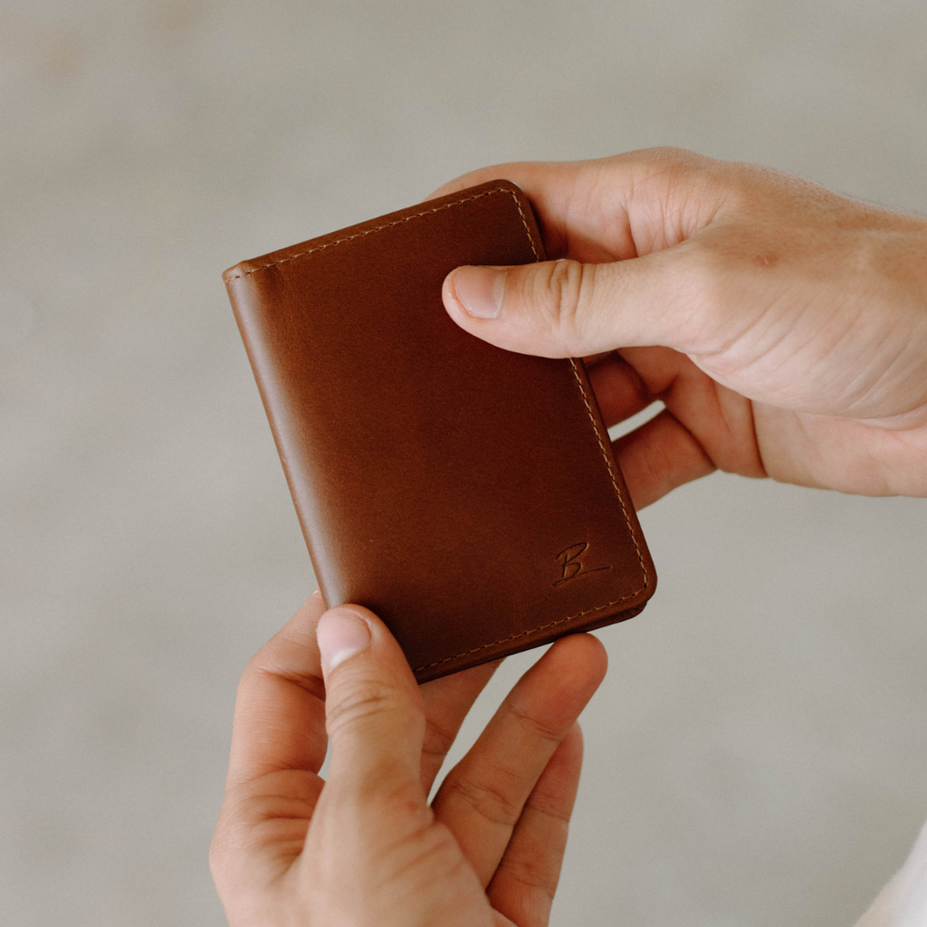 The Minimalist brown leather card wallet with embossed B held between two hands