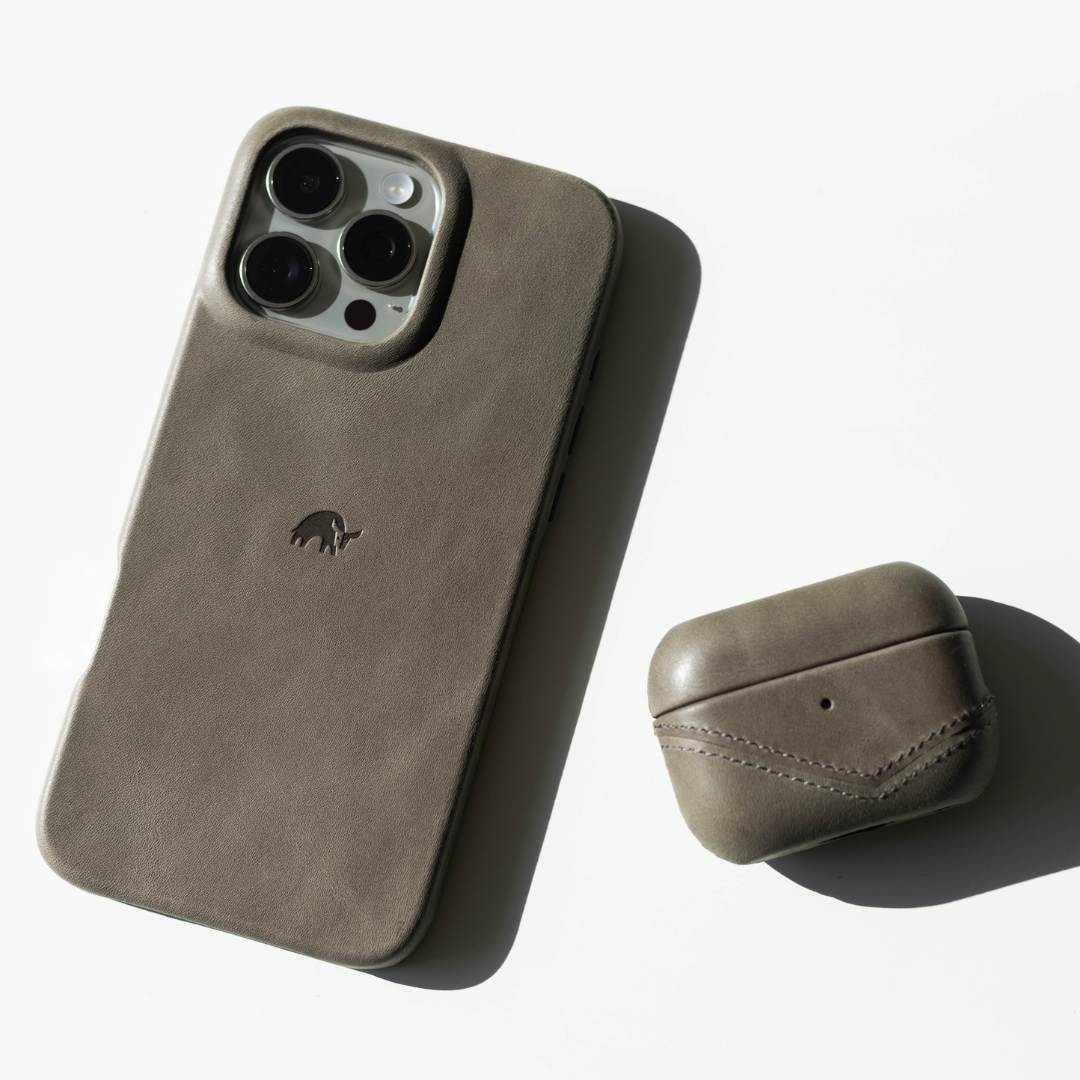 Gray-brown leather iPhone case with embossed elephant logo and matching AirPods case on white background, soft shadow.
