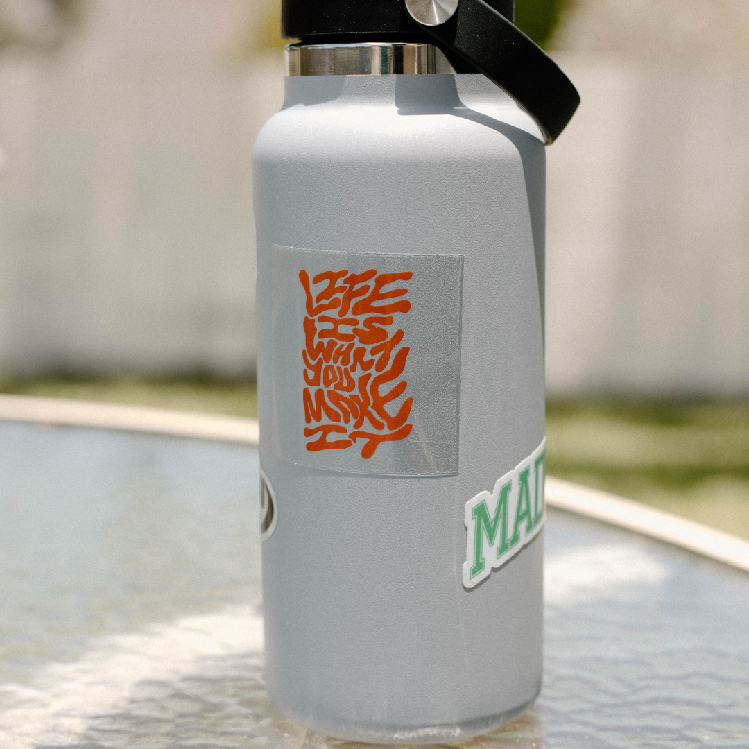 Gray insulated water bottle with an orange sticker reading 'LIFE IS WHAT YOU MAKE IT'.