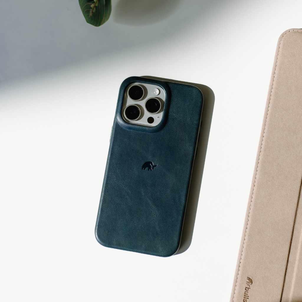 Teal leather iPhone case with three-camera cutout and small embossed logo, photographed on white surface.