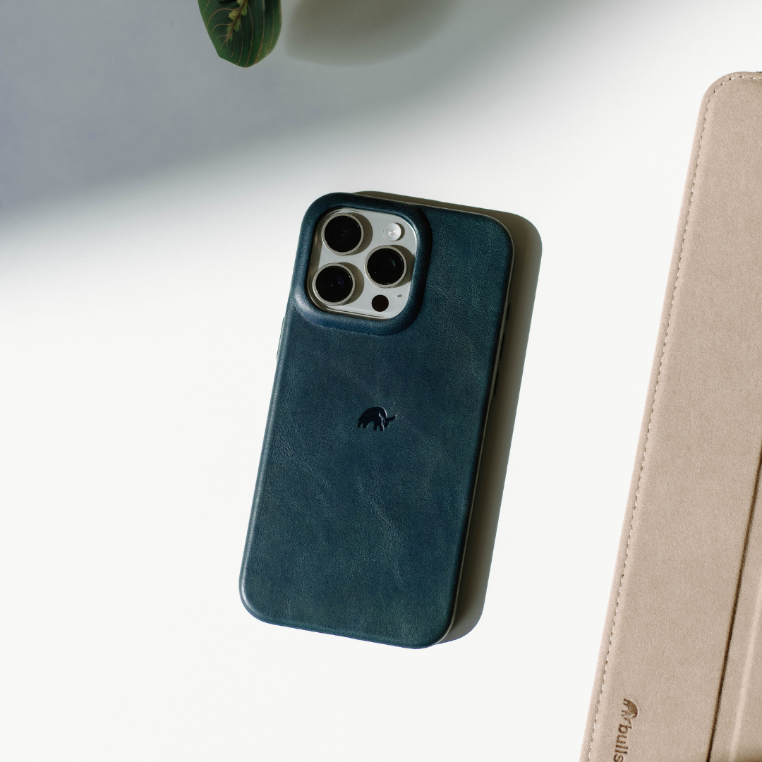 Teal leather iPhone case with three-camera cutout and small embossed logo, photographed on white surface.