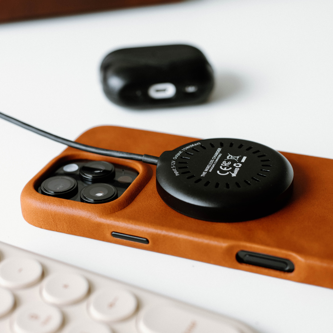 Black round wireless charging puck labeled THE WIRELESS CHARGER with FCC and CE marks on brown phone case, cable attached