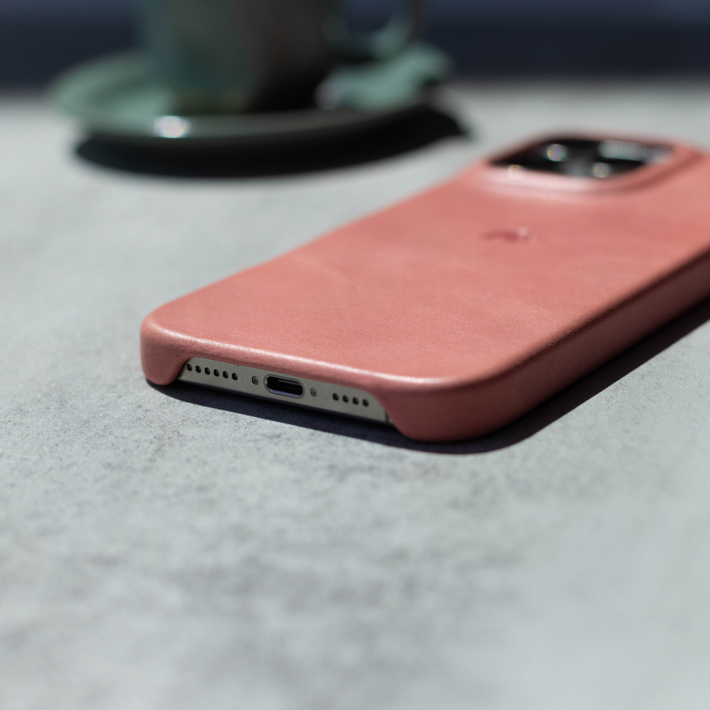 Pink leather iPhone case lying face down on a table, showing bottom Lightning port and camera cutout.