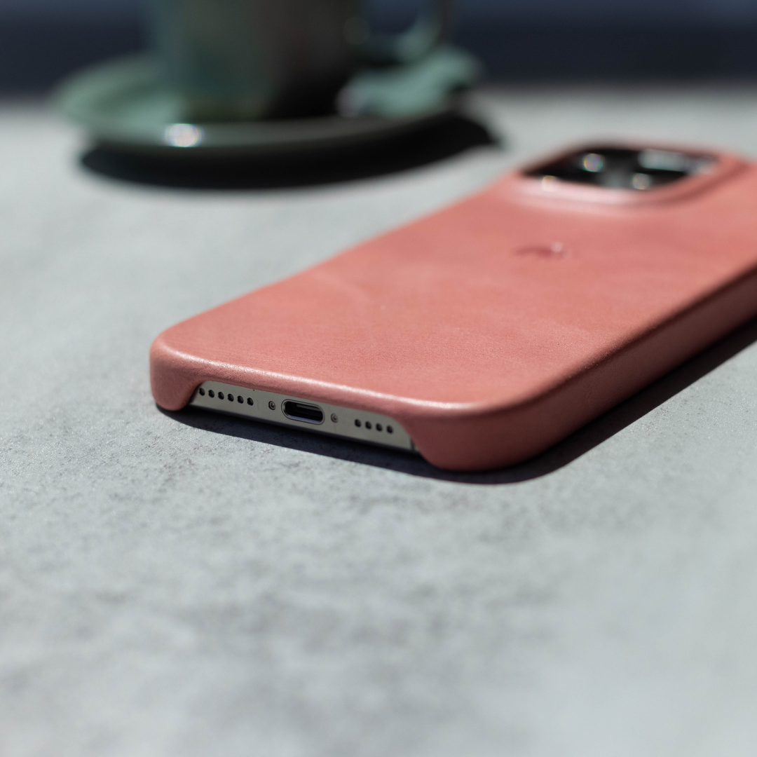 Pink leather iPhone case lying face down on a table, showing bottom Lightning port and camera cutout.