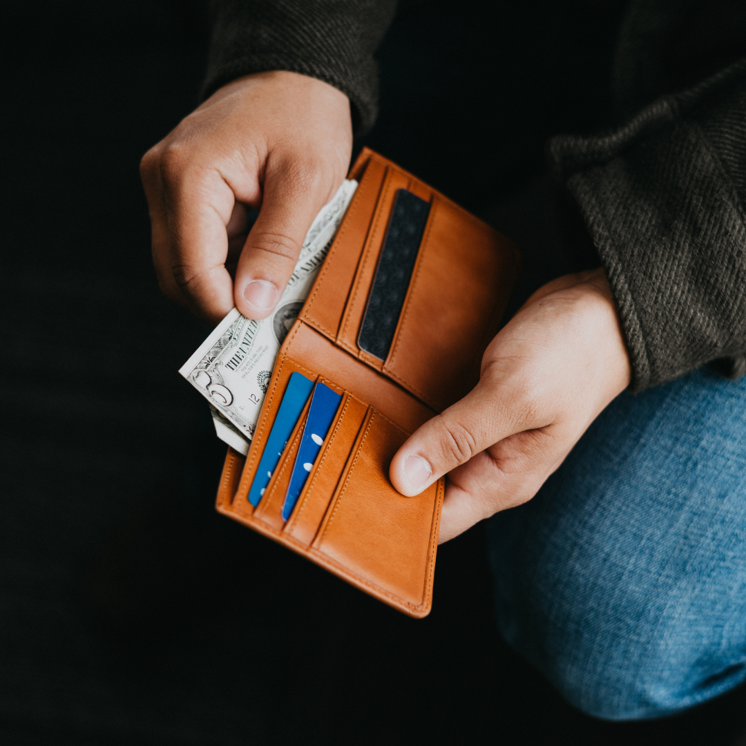 Sienna leather bifold wallet held open in hands, showing THE UNITED on a folded bill and two blue cards.