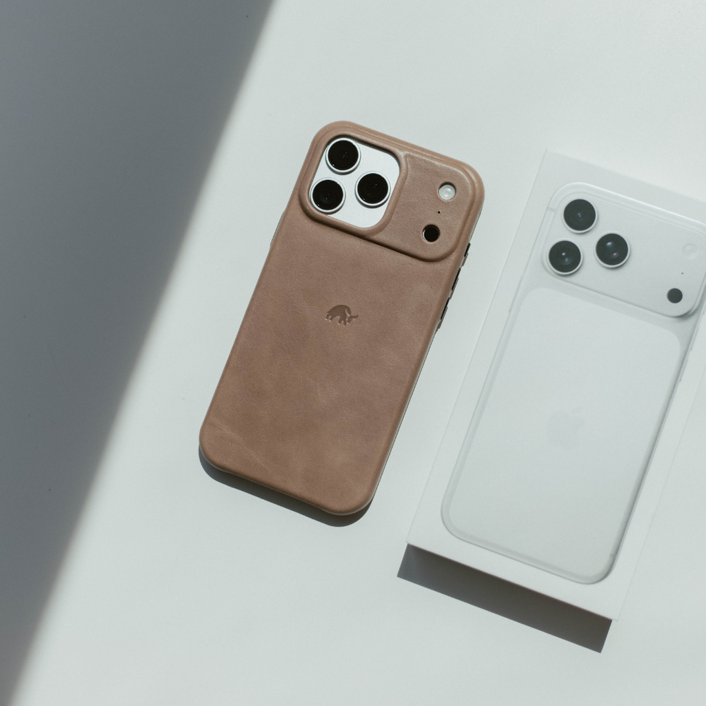 Tan leather iPhone case with small stamped elephant logo, lying beside a white iPhone box