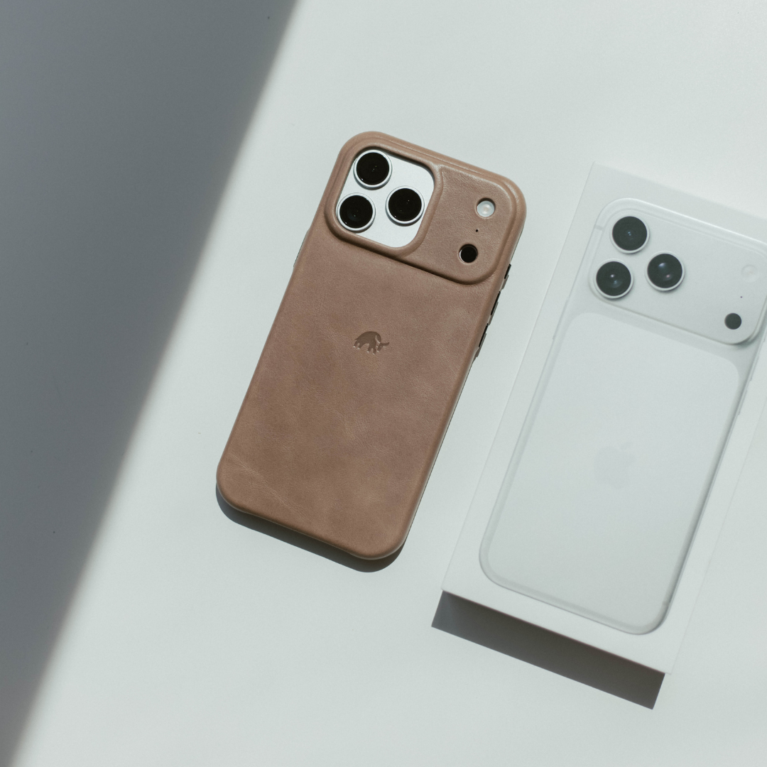 Tan leather iPhone case with small stamped elephant logo, lying beside a white iPhone box