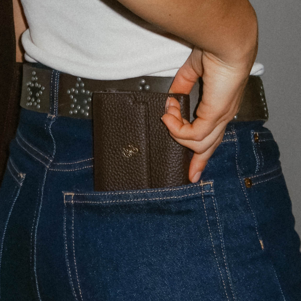 Hand sliding a textured dark wallet into the back pocket of blue jeans with a studded belt.