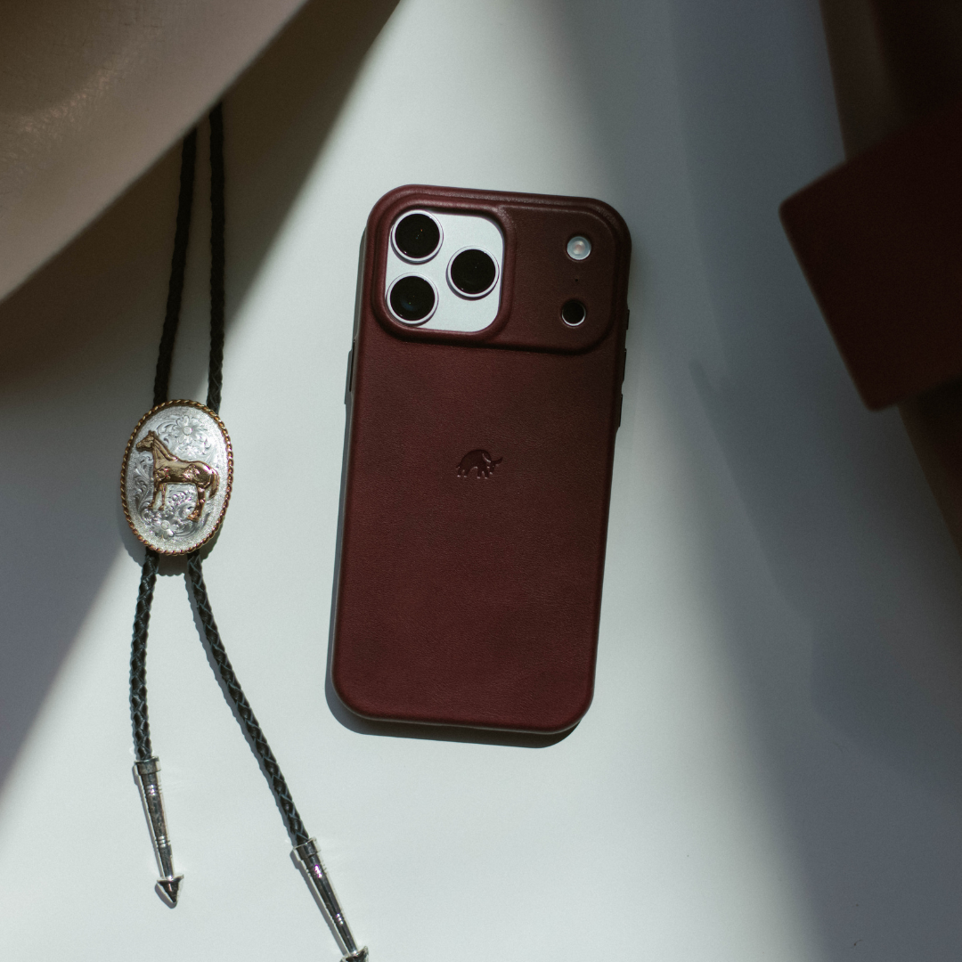 Bourbon leather Minimalist iPhone case lying flat beside a decorative bolo tie