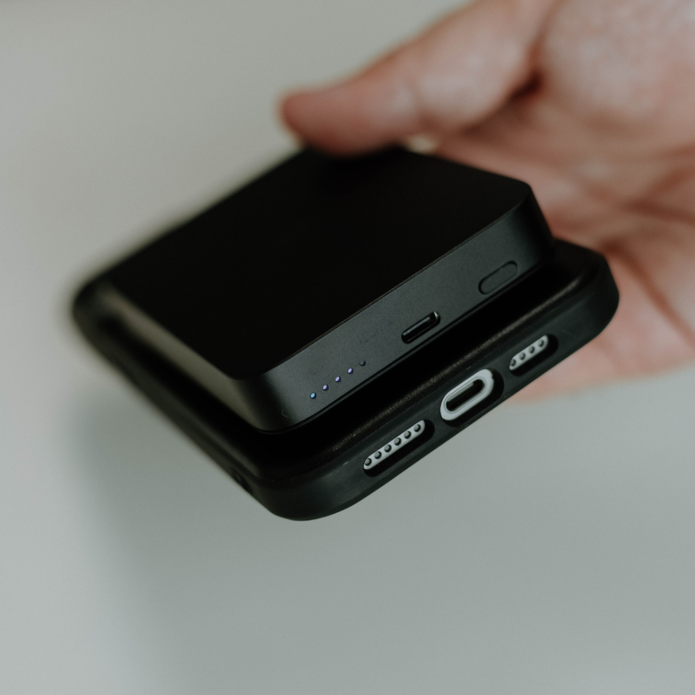 A hand holding the Bullstrap MagSafe Power Bank showing charging ports and indicator lights.