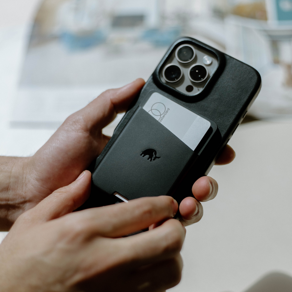 A person holding a black Magnetic Popper Wallet attached to an iPhone, showcasing its design and functionality.