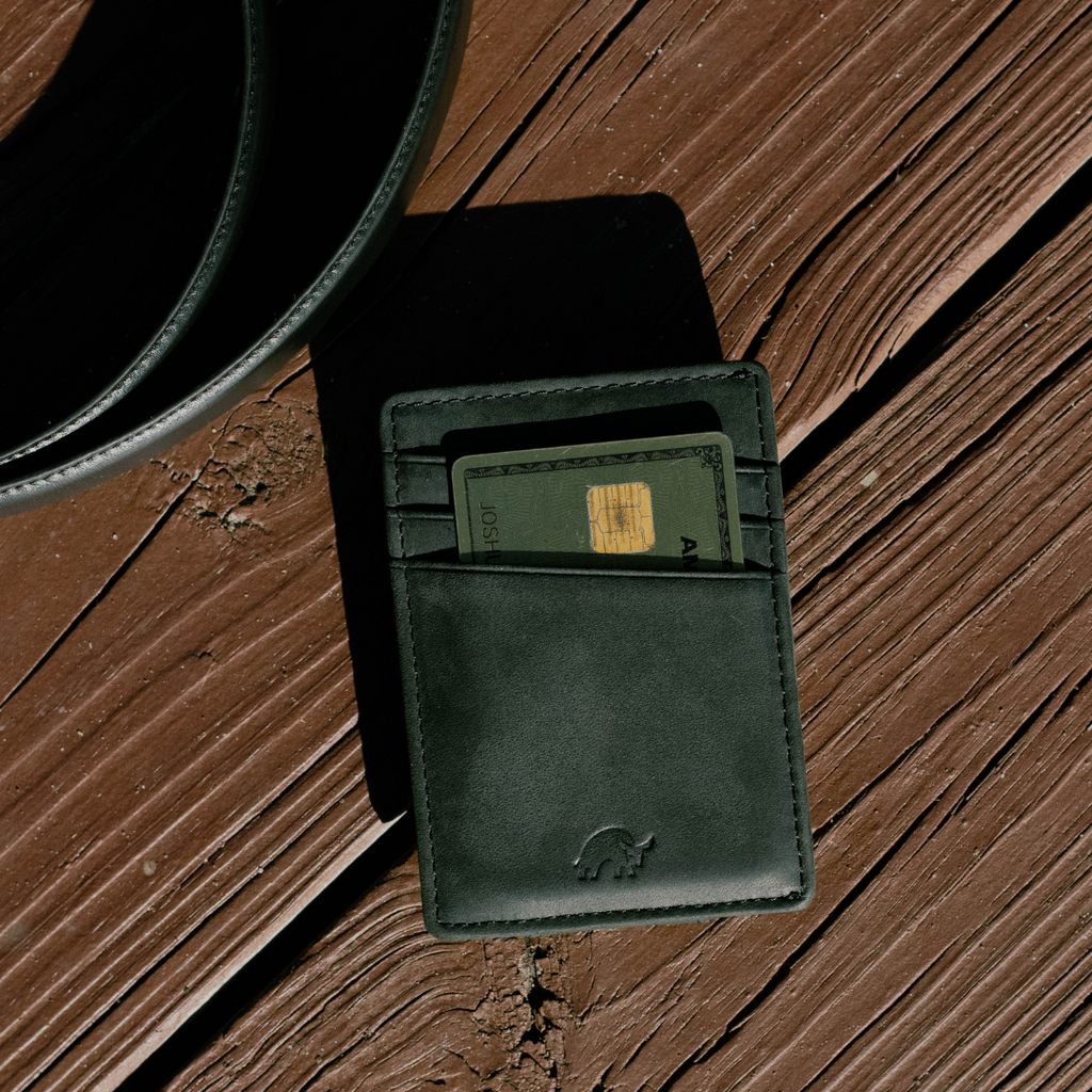 Black leather money clip wallet holding a card with visible gold chip, resting on weathered brown wooden planks